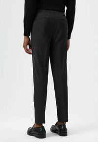 Op maat gemaakte donkergrijze broek met een gestructureerde afwerking, voorzien van een elastische tailleband, een slim-fit snit en twee achterzakken. Zwarte schoenen maken de look compleet.