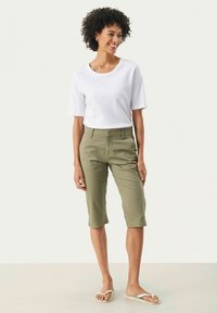 Tricou alb cu mânecă scurtă purtat cu pantaloni kaki până la genunchi și sandale albe, având o croială lejeră și o textură netedă.