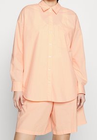 Peachfarvet bomulds skjorte med spidse kraver, frontknaplukning og en enkelt brystlomme, parret med matchende shorts.