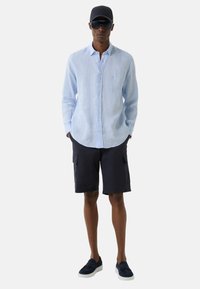 Lyseblå linned skjorte med lange ærmer, marineblå cargo shorts, marineblå slip-on sko, sort cap og solbriller. Enkel, afslappet outfit design.