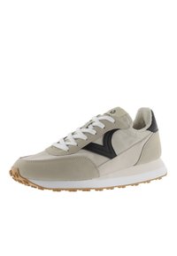 Scarpa sportiva beige realizzata in materiali scamosciati e pelle liscia, con lacci bianchi, dettagli neri e una suola in gomma testurizzata color cuoio.