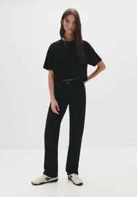 T-shirt noir court à manches courtes, associé à un jean noir taille haute et des baskets de couleur claire. Design simple et minimaliste.
