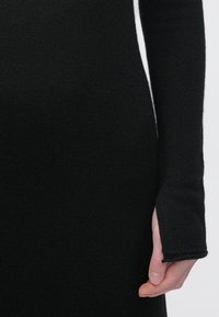 Czarna dzianinowa sukienka prezentująca teksturowaną tkaninę; dopasowany krój z długimi rękawami, z rozcięciem przy mankiecie i gładym wykończeniem.