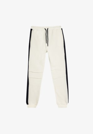 Cremefarvede joggers med sorte sidelister, lavet af blødt stof, med elastisk talje og to lynlåslommer.