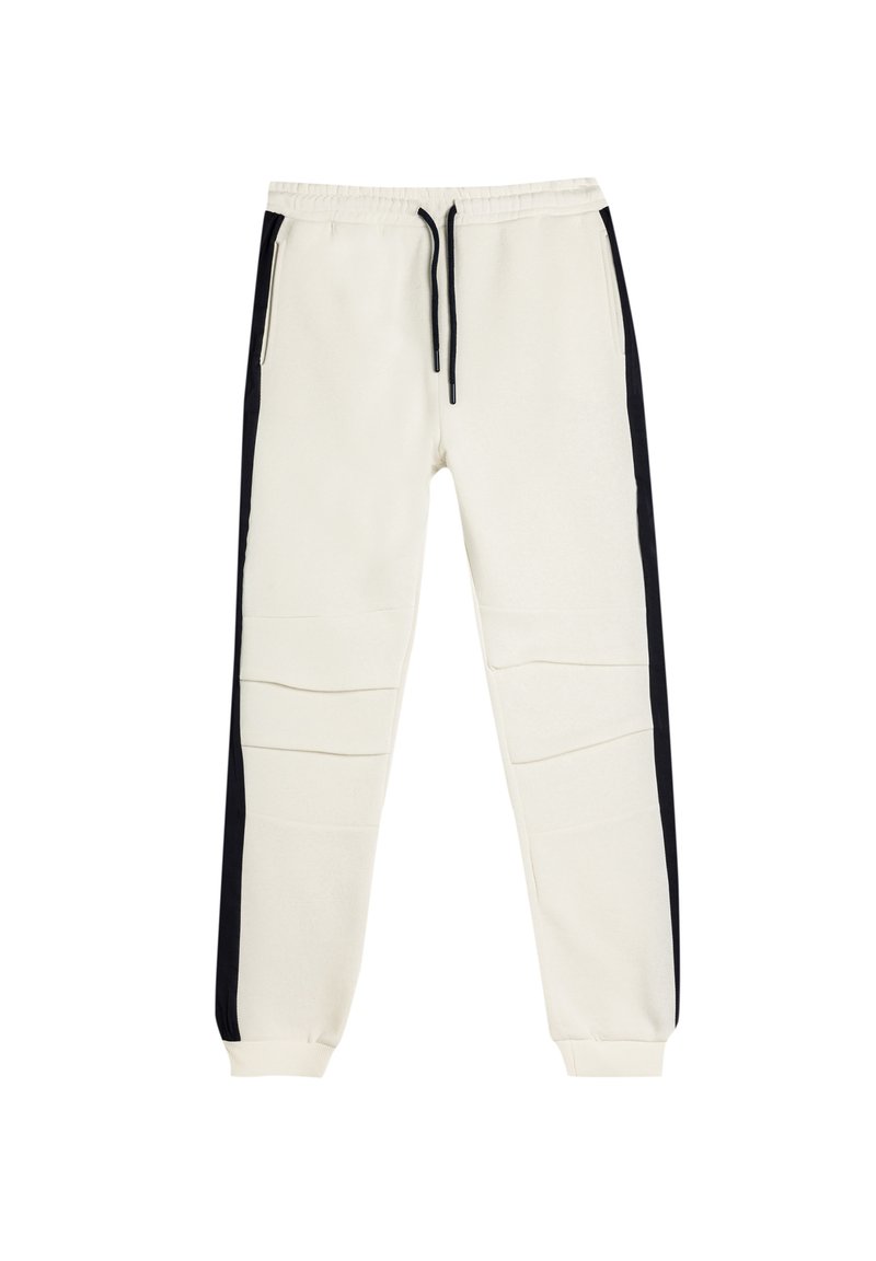 Cremefarvede joggers med sorte sidelister, lavet af blødt stof, med elastisk talje og to lynlåslommer.