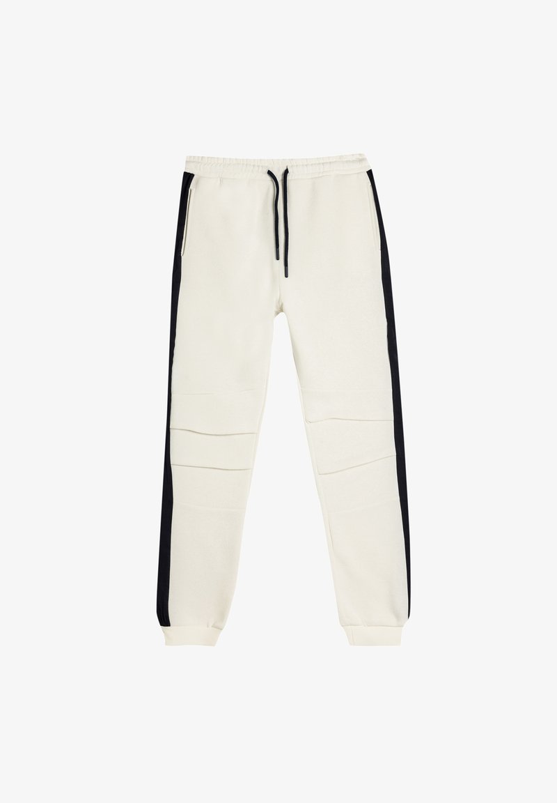 Cremefarvede joggers med sorte sidelister, lavet af blødt stof, med elastisk talje og to lynlåslommer.