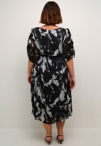 Zwart-wit geplooide jurk met een abstract patroon, een ingezette taille en zachte, luchtige mouwen. Bevat een sleutelgatdetail aan de achterkant.