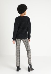 Black fluffy sweater with a relaxed fit, paired with gray plaid trousers featuring a slim cut and side stripes. Black block-heeled ankle boots.