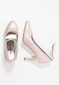 Scarpe con tacco alto in pelle sintetica rosa con finitura testurizzata, un accento argentato sul tacco e un design a punta aperta con una fascetta regolabile.