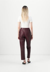 Bordeaux leren broek met een op maat gemaakte pasvorm, voorzien van een achterzak, en een soepele textuur, gecombineerd met een aansluitend wit top.