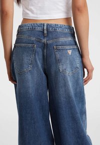 Weite Jeans aus mittelblauem Denim, mit hoher Taille, zwei Gesäßtaschen mit einem pinken, dreieckigen Logopatch und einem klassischen Nähdesign.