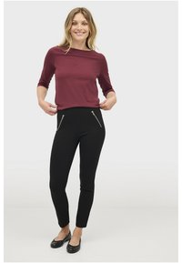 Bordeaux trekvartærmet top sat sammen med sorte slim-fit bukser med to lynlåslommer foran. Sorte flade sko fuldender looket.