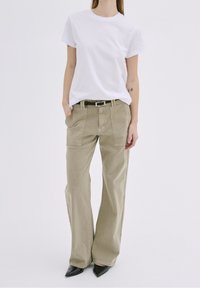 Beige široké nohavice s předními kapsami, v kombinaci s přiléhavým bílým tričkem. Černý opasek se stříbrnou sponou dotváří outfit.