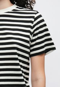 Črno-bela črtasta majica z okroglim izrezom in kratkimi rokavi. Mehka tkanina z običajnim krojem in vidnimi detajli šivov.