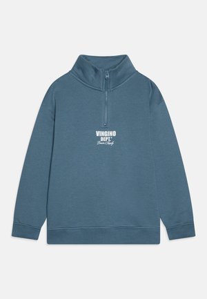 En zip-up hettegenser i dempet blå med høy krage og lange ermer. Har et hvitt trykt logo på brystet og ribbestrikkede ermer.