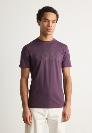 Camiseta de algodón morada con cuello redondo y mangas cortas. La parte frontal muestra un gran logo sutil en un tono contrastante.