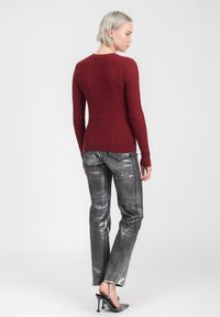 Dieprode geribde lange mouw top gecombineerd met metallic grijze slim-fit broek. Schoenen zijn zwart met een puntige neus en een met kralen versierde band aan de achterkant.