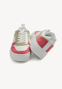 White sneakers with pink and green suede accents, metallic gold hardware, and a thick white rubber sole. Features laces and a rear pull tab.