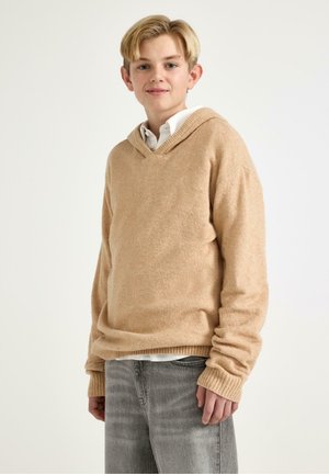 Beige hættetrøje lavet af blødt, tekstureret stof med V-hals, ribstrikkede manchetter og kant, kombineret med grå jeans.