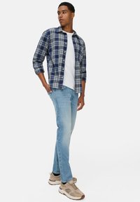Geruite shirt in blauw en wit, over een wit t-shirt gedragen. Lichtblauwe jeans en beige sneakers maken de look compleet. Casual pasvorm en ontwerp.
