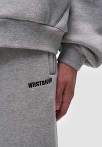 Šedá mikina a odpovídající tepláky vyrobené z měkké látky, na noze kalhot s černým vyšitým textem "WRSTBHV". Ležérní design.