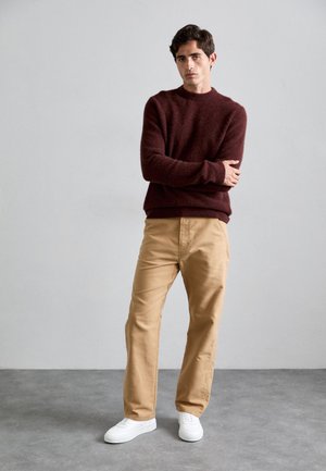 Pull en laine bordeaux avec un col rond, pantalon en coton kaki et baskets blanches. Texture douce, coupe décontractée et design simple.