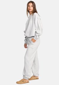 Grauer Sweatshirt und passende Jogginghose aus weichem Baumwoll-Mischgewebe. Lockere Passform mit gerippten Bündchen. Braune Clogs zum Hineinschlüpfen runden das Outfit ab.