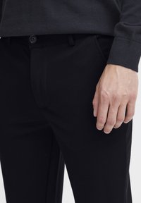 Schwarze maßgeschneiderte Hosen aus glattem Gewebe, mit einem frontalen Knopfverschluss, seitlichen Taschen und einem schlanken Schnitt.