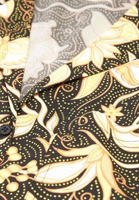 Tessuto nero con intricate fantasie floreali gialle e bianche, caratterizzato da una trama liscia e un dettaglio con bottone. Visibili due strati di tessuto.