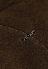 Hnědý semišový materiál s hladkou texturou, zdobený kovovým logem "wojas" a jemnými šitími detaily.