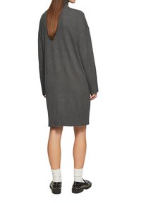 Robe tricotée grise avec un col montant, des manches longues et un ourlet côtelé. Portée avec des chaussettes blanches et des chaussures noires ornées. Silhouette simple et décontractée.