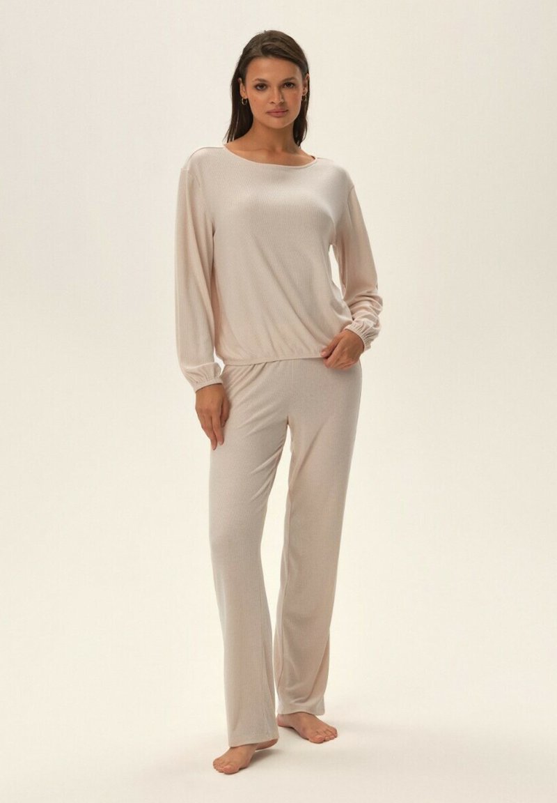 Jasnoróżowy zestaw piżamowy o prążkowanej strukturze. Zawiera bluzkę z długim rękawem o okrągłym dekolcie oraz pasujące długie spodnie o luźnym kroju.