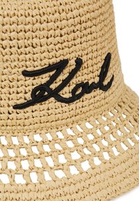 Kootud heina ämbrimüts beežis, mis on hingava avatud mustriga. Esiküljel musta värvi tikitud "Karl" logo.