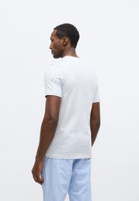 Svetlomodra bombažna majica s kratkimi rokavi, okroglim izrezom, mehka tkanina, sproščen kroj, nošena s kockastimi modrimi pižamnimi hlačami, enobarvno ozadje.