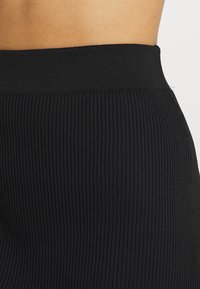 Schwarze, gerippte, hoch taillierte Leggings mit einer strukturierten Oberfläche und elastischem Bund, die ein figurbetontes Design präsentieren.