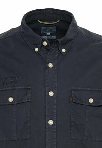 Marineblaue button-up Hemd mit Kragen, weißen Knöpfen, zwei Fronttaschen und gesticktem Text "CONNECT 1977" auf der linken Seite.