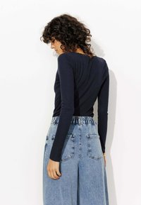 Haut à manches longues bleu marine associé à un pantalon en denim léger à taille haute et coupe ample, doté d'une taille élastique et de deux poches arrière.