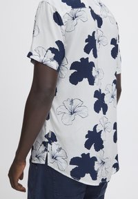 Camicia a maniche corte in tessuto leggero con grande motivo floreale di hibiscus blu navy, con contorni bianchi, spacchi laterali e taglio dritto.