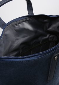 Bolso de mano azul marino con exterior de tela texturizada y detalles de cuero liso. La abertura con cremallera revela un interior negro con un bolsillo.