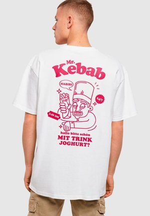 T-shirt en coton blanc avec un imprimé graphique rose d'un chef tenant un kebab, avec du texte et des détails de style cartoon. Design ample et décontracté.