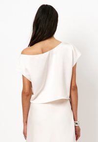 Lichtbeige off-shoulder top met korte mouwen, een gladde textuur en een relaxte pasvorm, gecombineerd met een bijpassende rok die zichtbaar is op de taille.