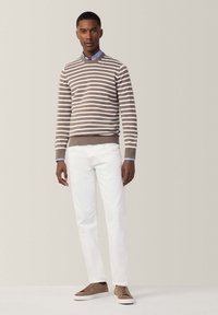 Maglione a righe marrone e bianche, camicia colletto azzurro, pantaloni bianchi e sneakers marroni. Look casual con polsini e vita a coste.