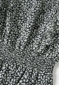 Tissu noir et blanc avec motif abstrait de feuilles, taille élastiquée froncée et détail volanté sur un matériau léger.