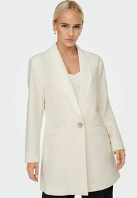 Blazer long blanc avec une coupe ajustée, cols crantés, fermeture à un bouton, deux poches avant et une texture lisse. Stylisé sur un haut.