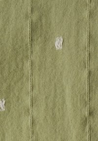 Tessuto verde oliva con una superficie texturizzata, caratterizzato da accenti ricamati bianchi. Linee di cucitura distintive creano un motivo strutturato.