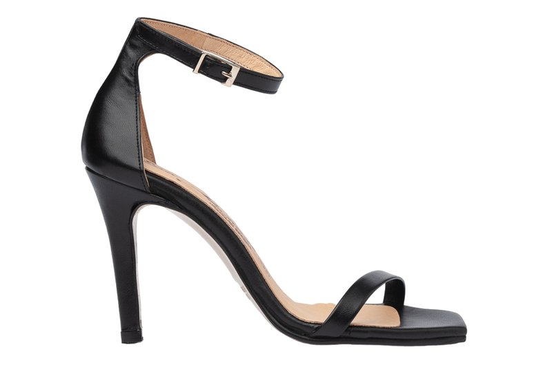 Sandalia de tacón alto con tira en el tobillo de cuero negro y un diseño elegante, que presenta un tacón delgado y una única banda para los dedos del pie. La suela es de un color claro en contraste.