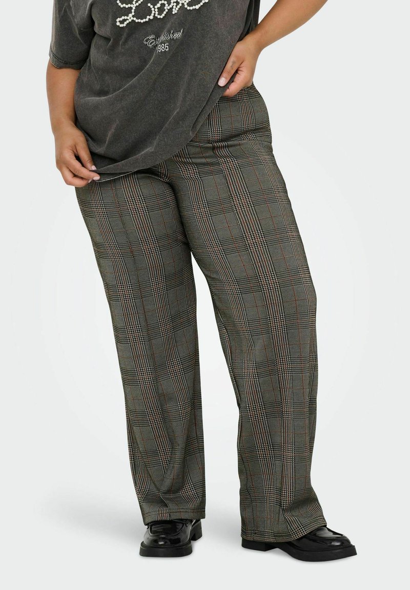 Pantalons larges à carreaux dans des tons de vert atténué, blanc et rouge ; fabriqués dans un tissu texturé. Portés avec un t-shirt graphique gris ample et des chaussures noires.
