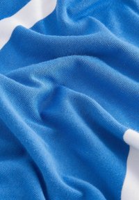 Niebieska teksturowana tkanina z jasnoniebieskimi i białymi paskami, ukazująca miękki materiał dzianinowy i widoczne zagniecenia. Lekka i gładka w wyrazie.