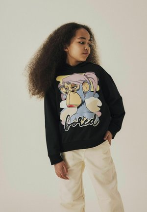 Svart sweatshirt med en färgglad apa-grafik med rosa detaljer och ordet "loved" i glänsande tryck. Ljust färgade byxor fulländar outfiten.