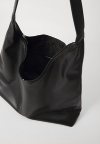 Svart läderhandväska med en slät yta, som har en stor öppen topp och ett dragkedjestängning. Insidan är fodrad med svart tyg.